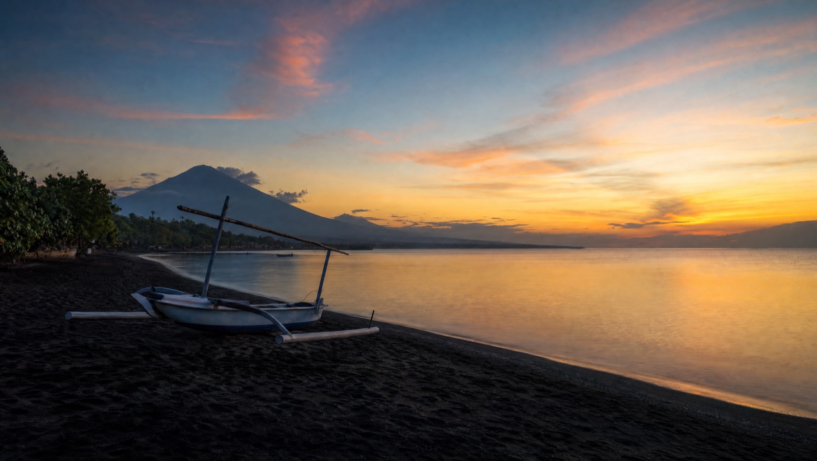 Black-sand beach on Bali's north coast at dawn with a jukung outrigger