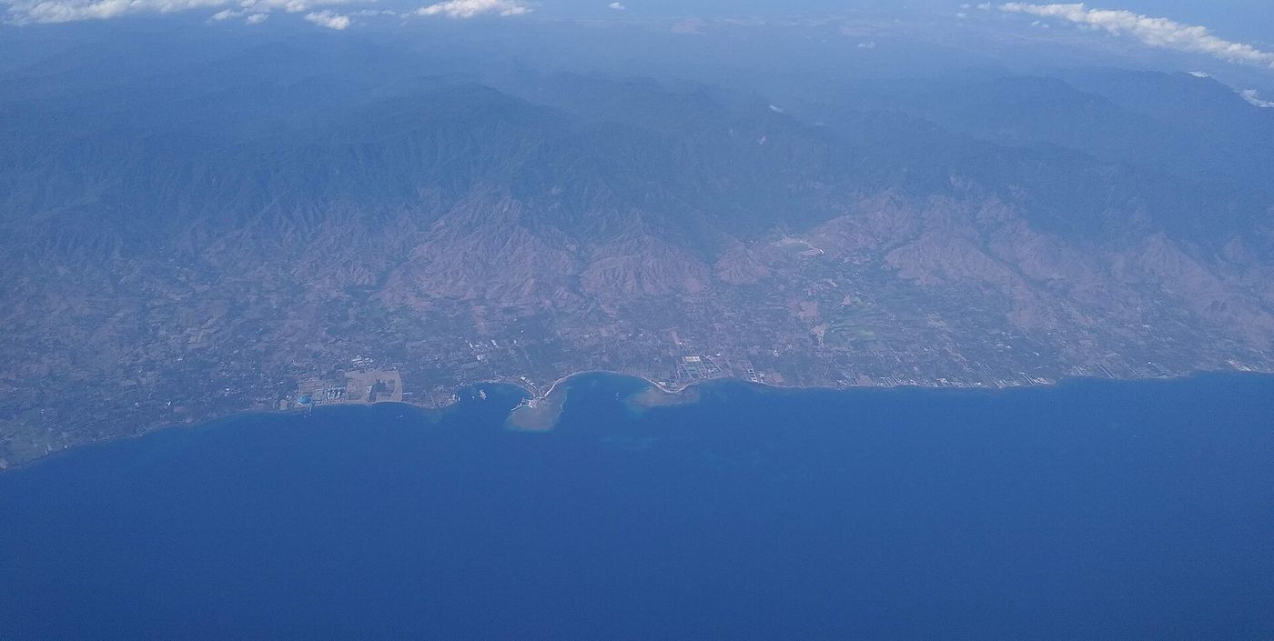 Buleleng's north coast from the air, dry hills rising behind a string of bays, a harbour and coastal villages