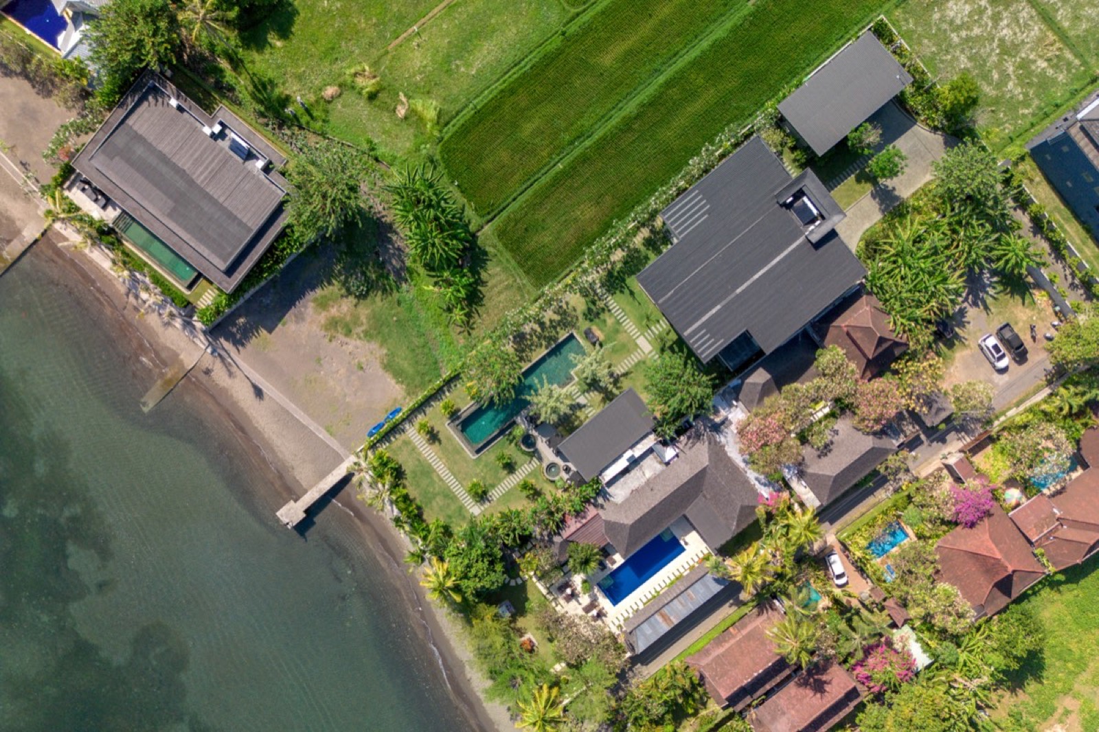The Lovina shore from directly above: a pier, black-sand beach, villa gardens and rice fields side by side