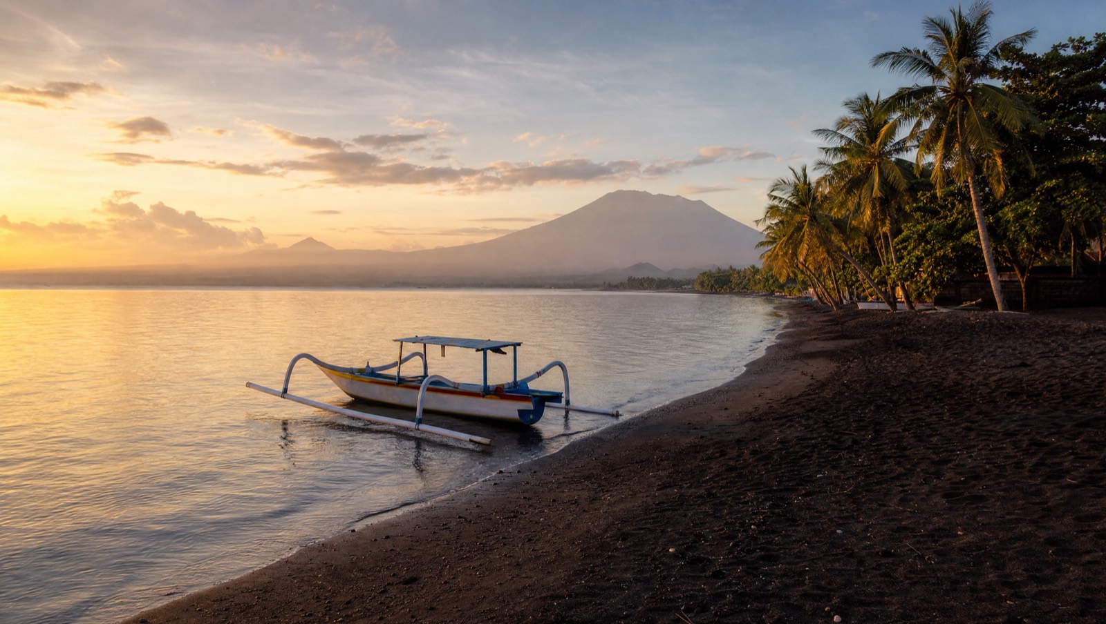 Calm black-sand north Bali beach with shallow water, family-friendly