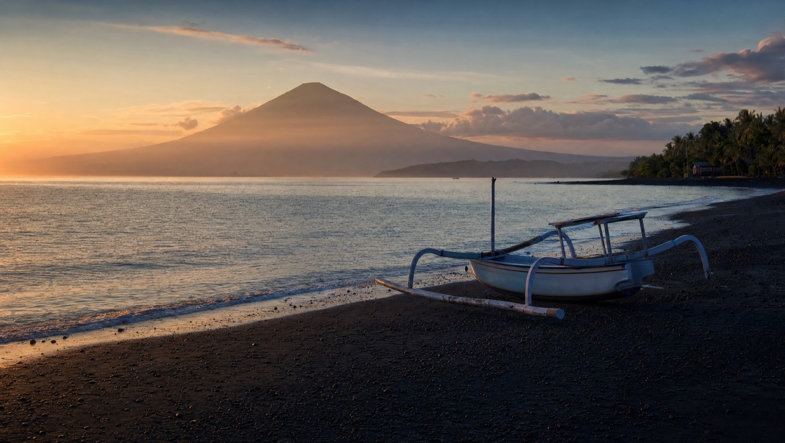 Serene north Bali black-sand coast at dawn with a jukung boat