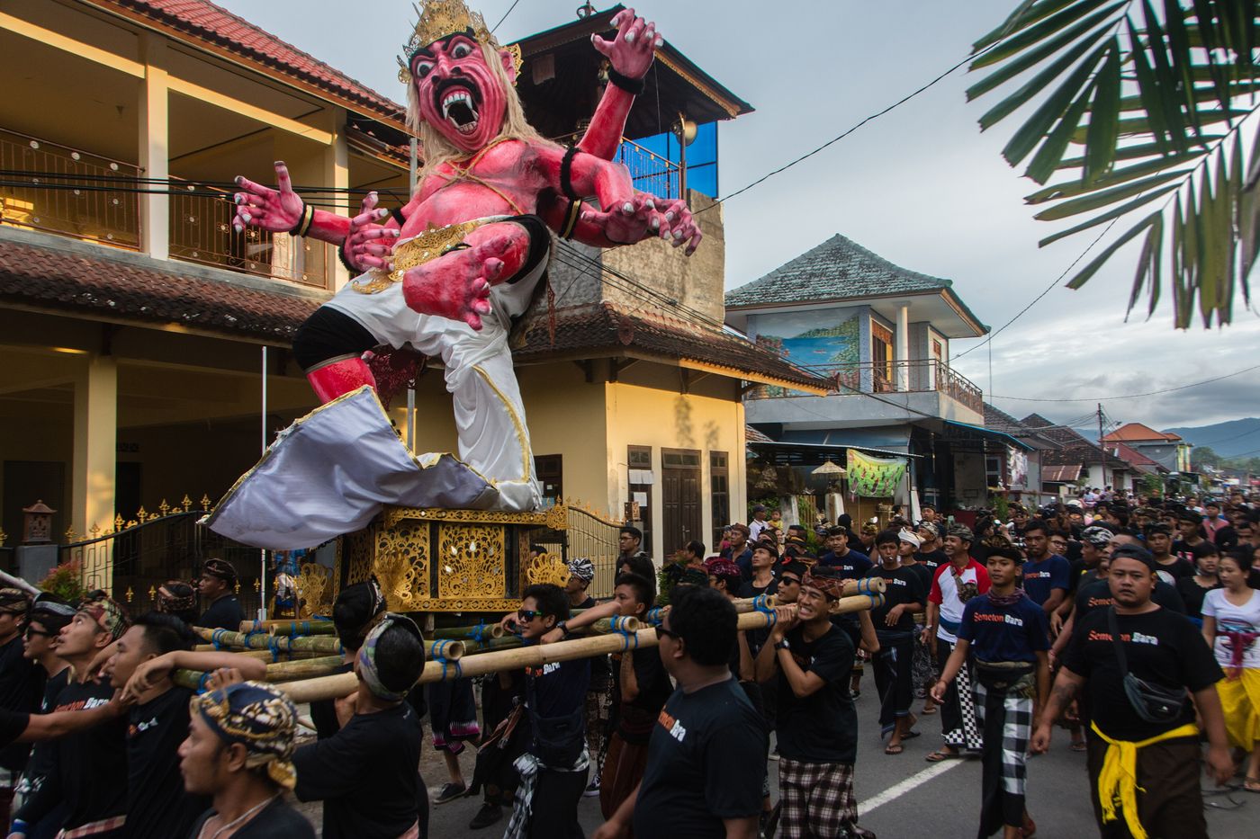 Young men carrying a towering pink demon ogoh-ogoh on a bamboo platform through a village street on the evening before Nyepi