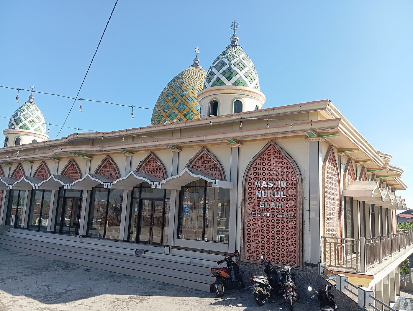 Masjid Nurul Islam in Seririt, its green and gold tiled domes above a red lattice facade signed Seririt Bali