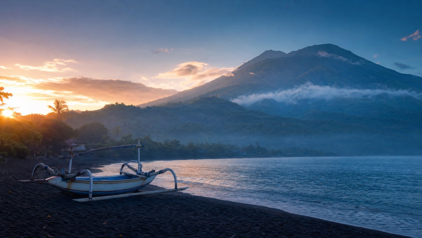 North Bali black-sand coast at dawn with a jukung boat and green hills