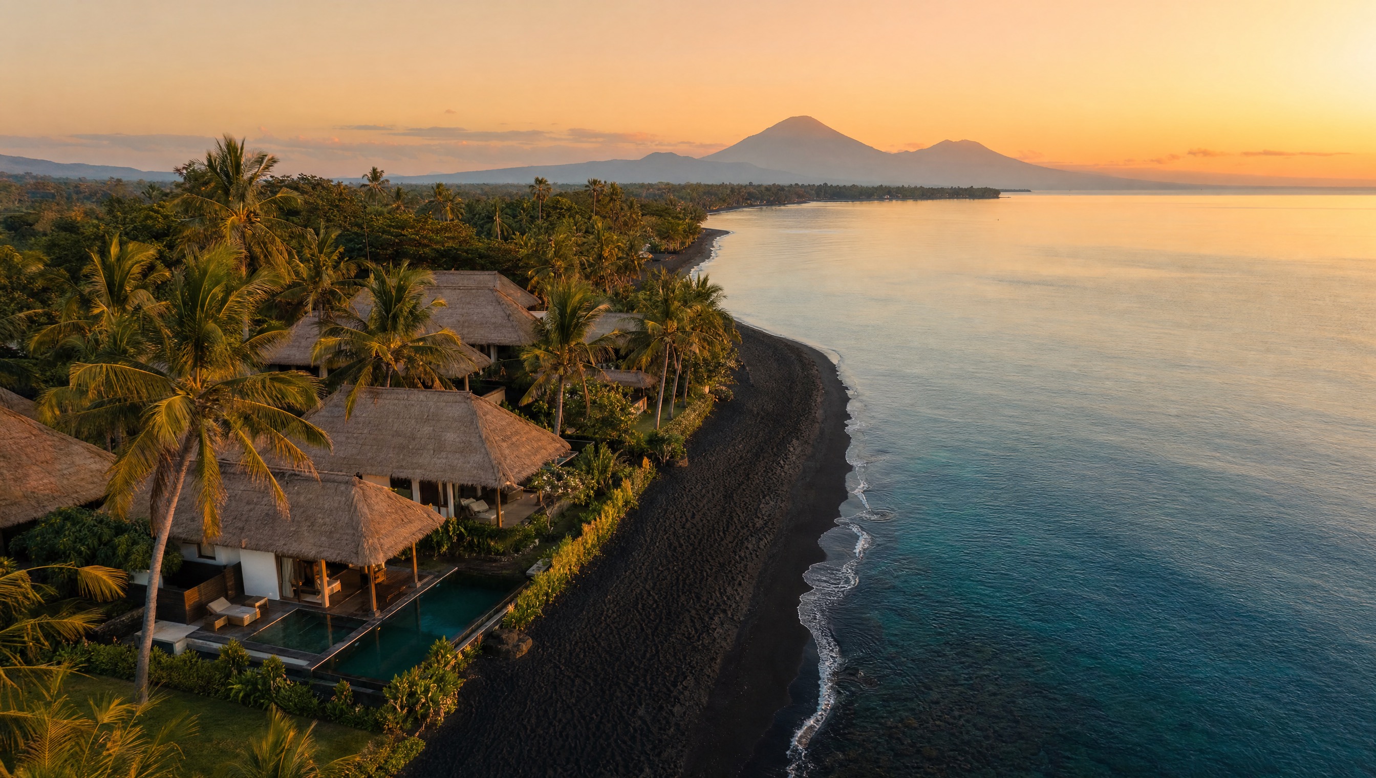 Aerial view of the calm black-sand north Bali coastline with villas among palms