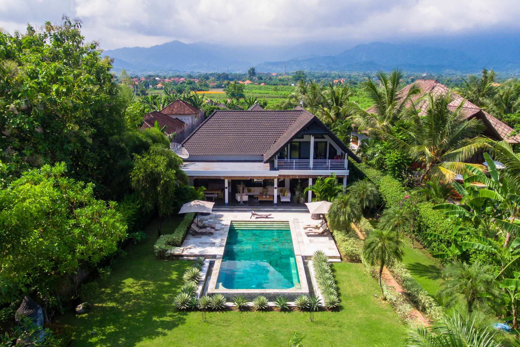 Villa Mahkai's pool and garden from the air, rice fields and the north Bali mountains behind
